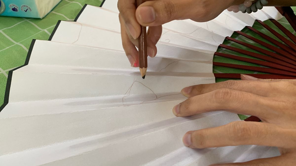 Hand sketching on a blank white fan with a pencil