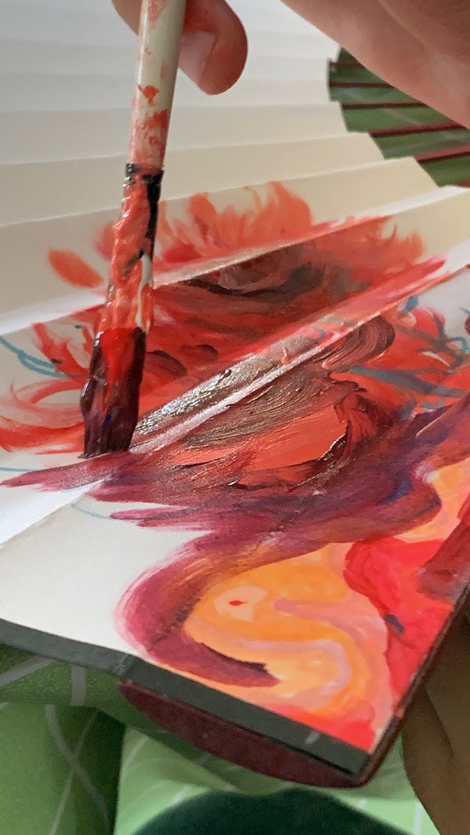 Brush painting red and orange swirls on a fan